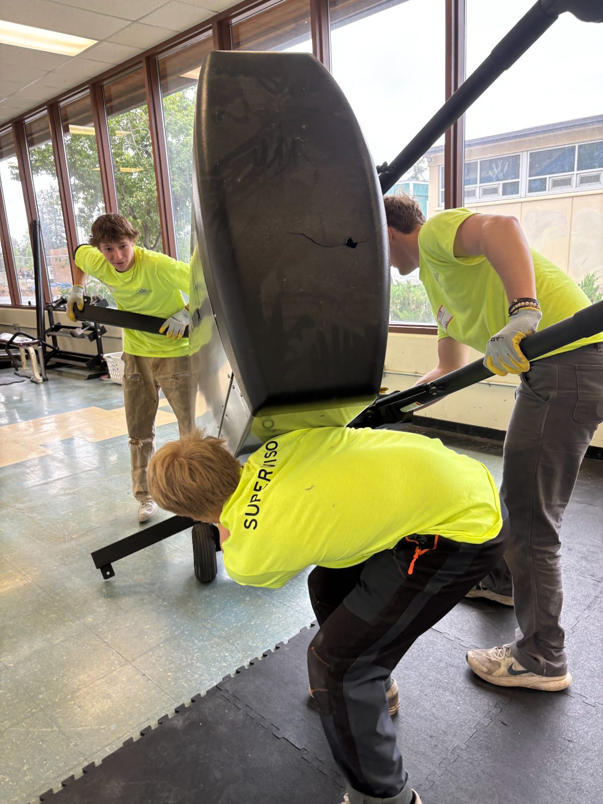 Crew members moving heavy gym equipment indoors